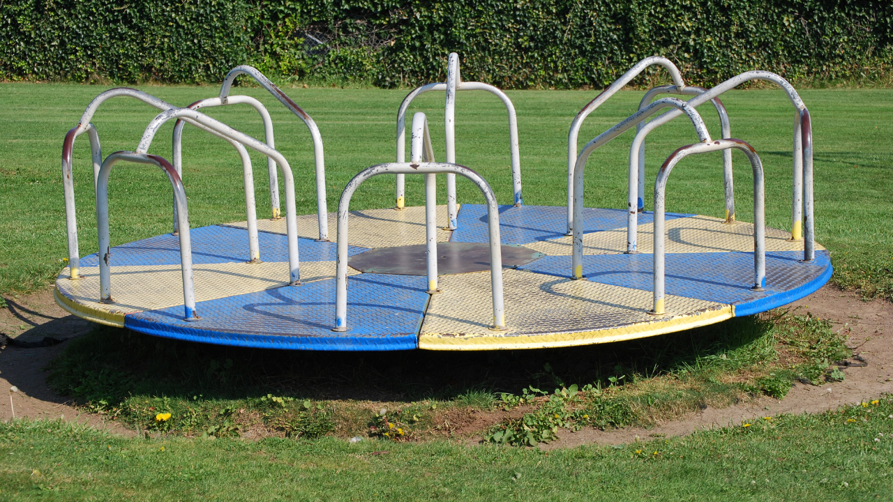 A vintage playground merry-go-round spinning with children, highlighting its nostalgic design and cultural significance.