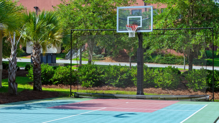 Outdoor basketball court with hoop, surrounded by greenery, showcasing court features and design.