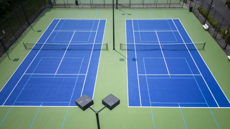 Renovation process of hard tennis courts with construction equipment and new surface materials.