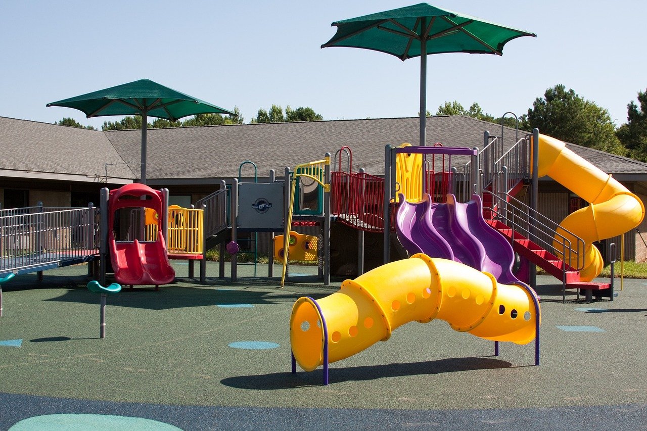 Children playing on colorful, safe play equipment in a park or playground.