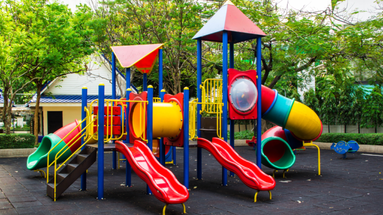 Children playing on various types of playground equipment in a park, including swings, slides, and climbing structures.