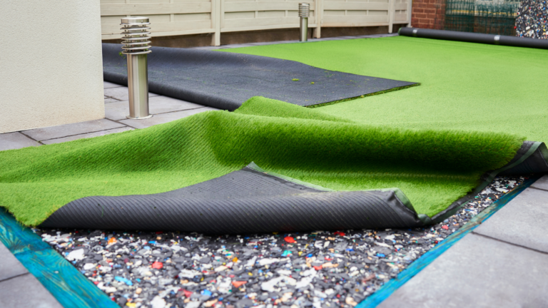 A person using a brush to smooth out lines or creases on a section of artificial turf.